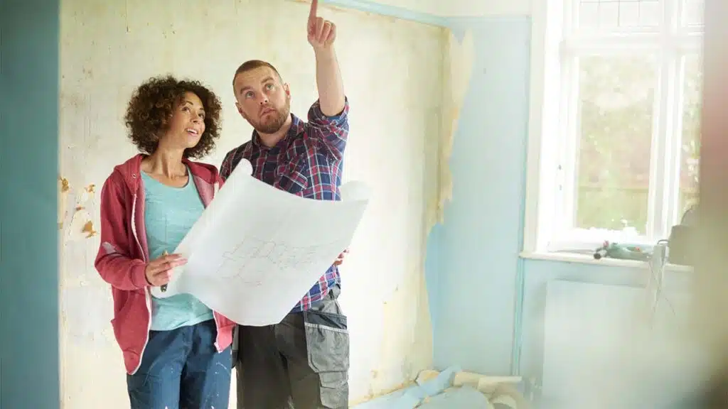 A couple stands in a partially renovated room, discussing home improvement plans