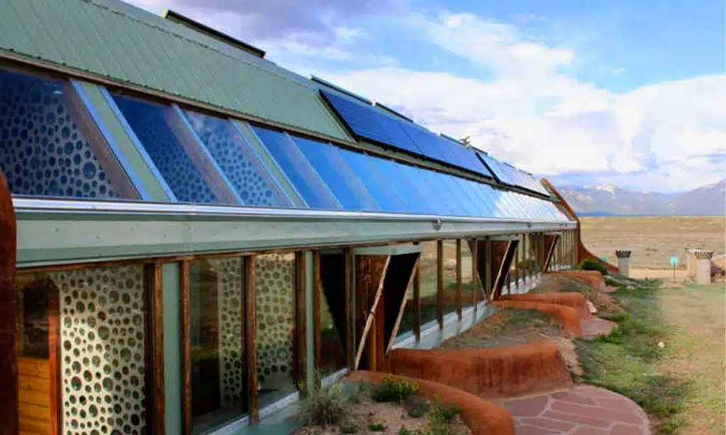 Eco-friendly earthship home with slanted solar panels and large windows designed for passive solar heating