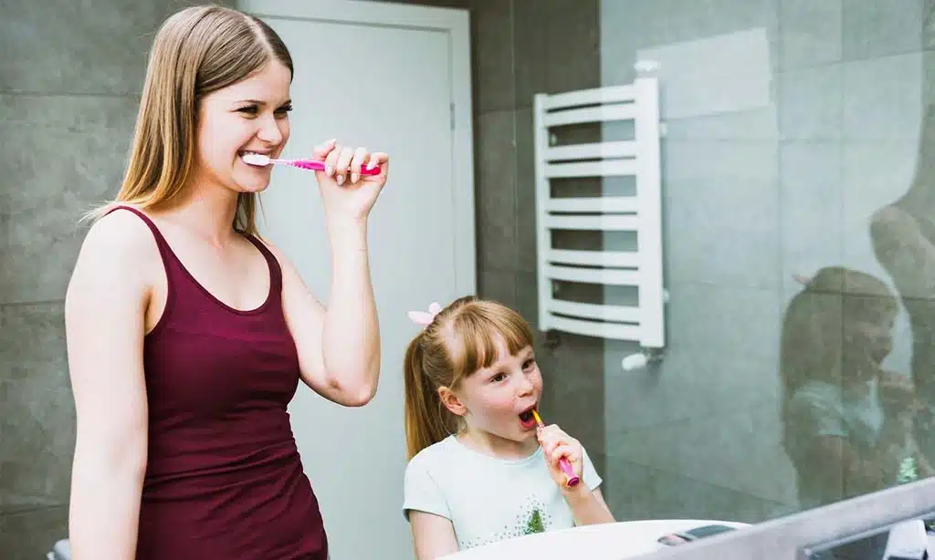 Mother and daughter brushing their teeth together in the bathroom.