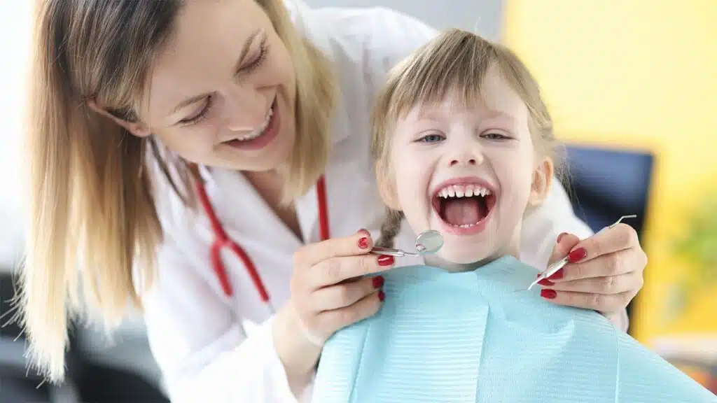 A cheerful dentist examines a happy child's teeth during a check-up