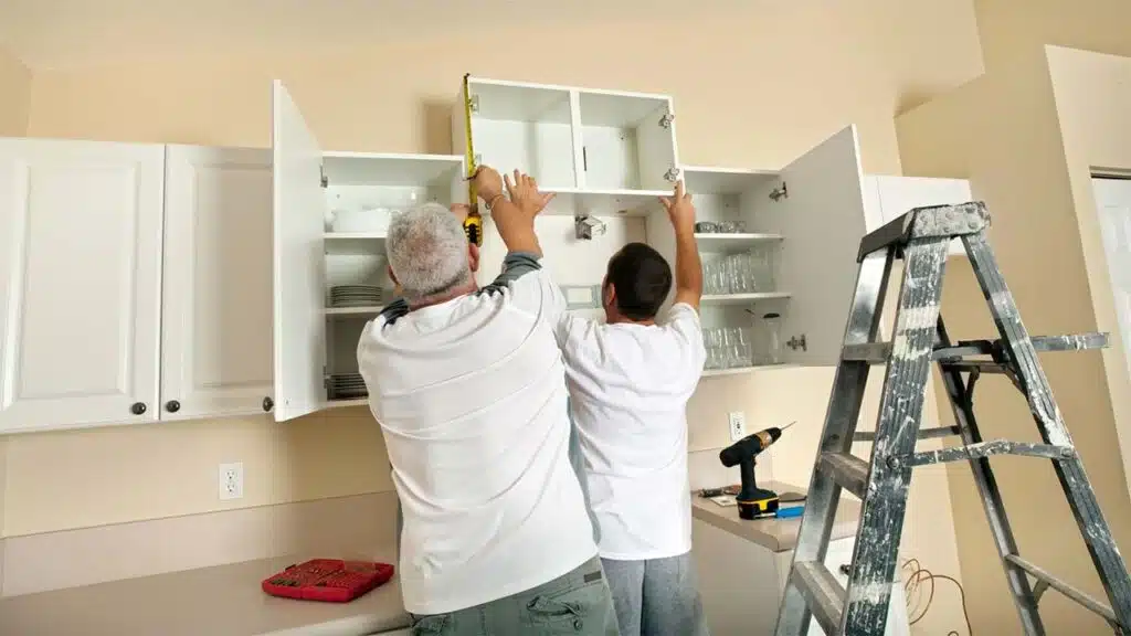 Two people are installing kitchen cabinets