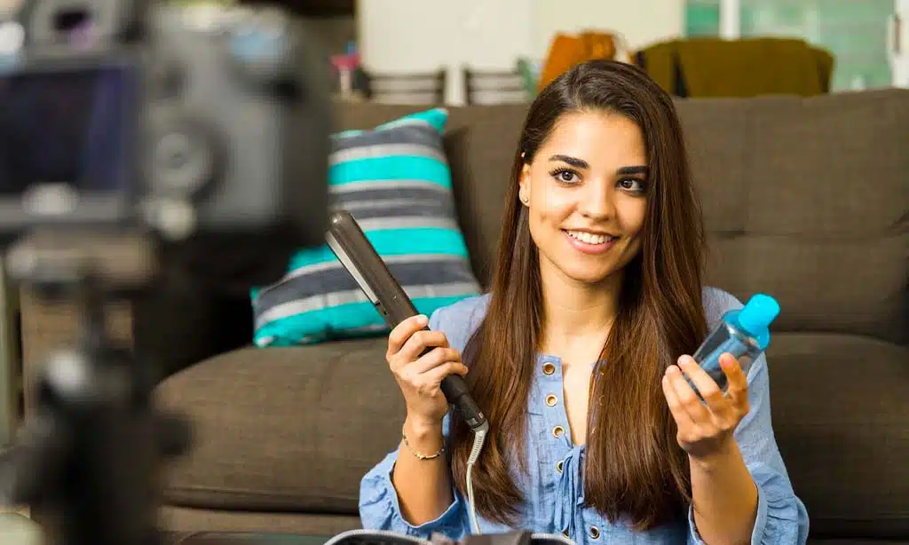 Young woman recording a beauty tutorial at home, showcasing hair products for social media content creation.