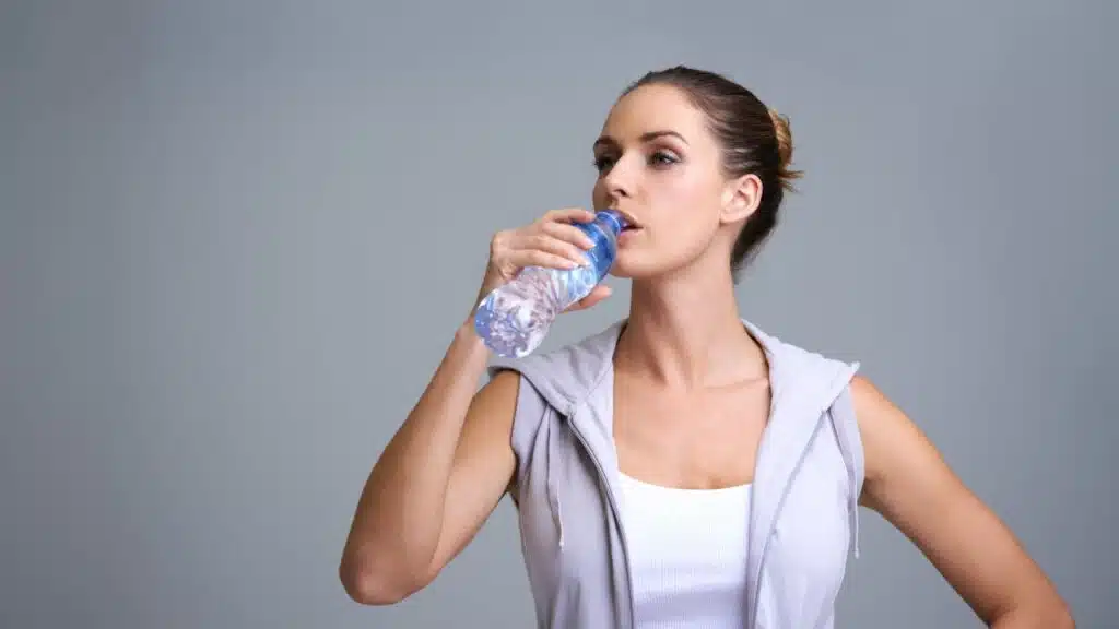 A woman in athletic attire taking a sip of water from a plastic bottle