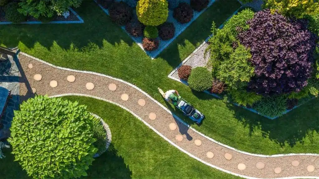 An aerial view of a landscaped garden with a person mowing the grass