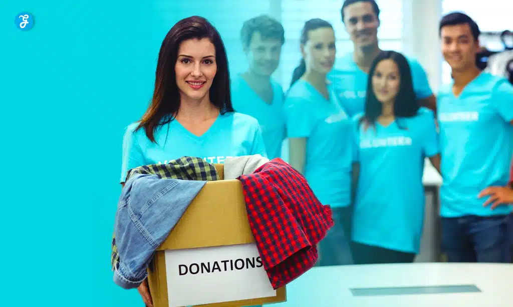 Group of volunteers, with a woman in the foreground holding a donation box filled with clothes