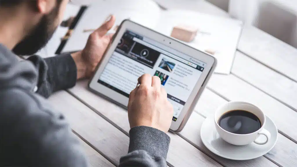 Person reading online content on a tablet with a cup of coffee on the table, browsing the internet.