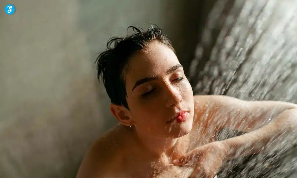 A person taking a shower, their eyes closed as they enjoy the water streaming down