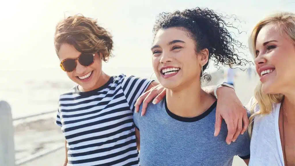 Three Happy Friends Laughing Together Outdoors by the Beach