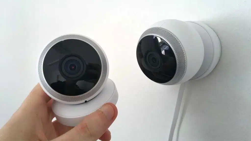 A person holding a small, round security camera near another one mounted on a wall.