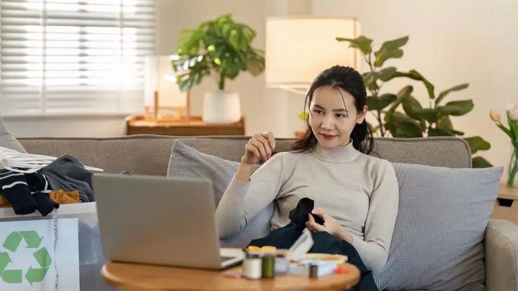 Woman sewing clothes at home while watching a tutorial on her laptop