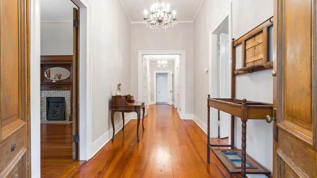 A classic hallway with polished wooden floors and soft cream walls, illuminated by elegant chandeliers