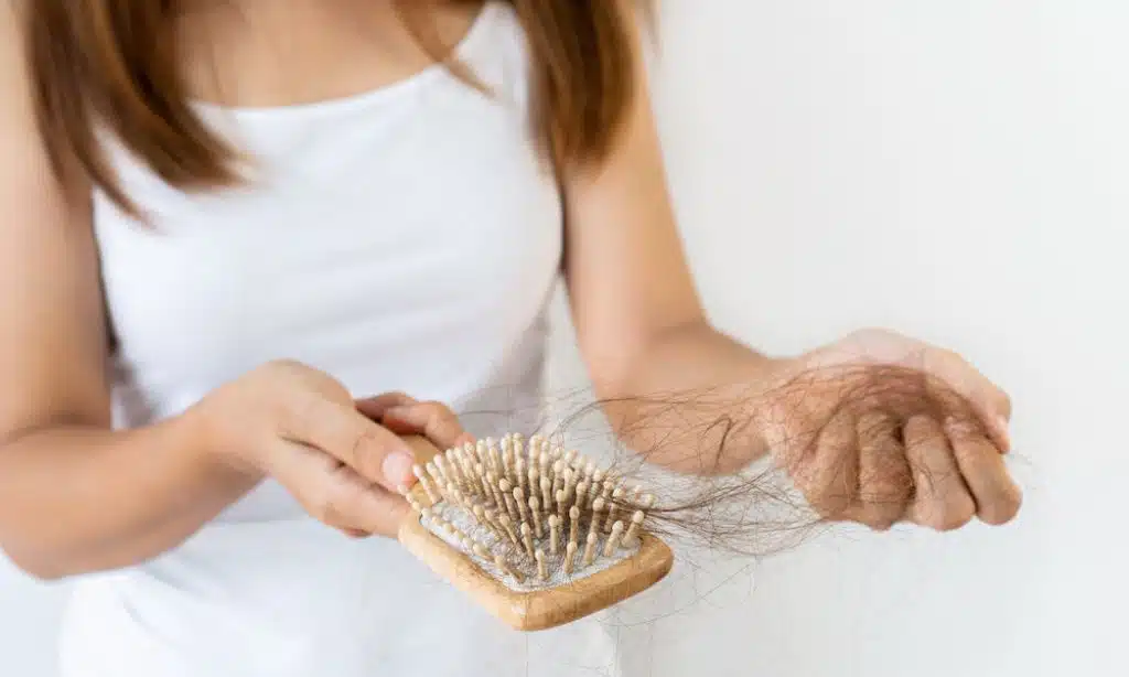 A woman pulling hair strands out of her hairbrush