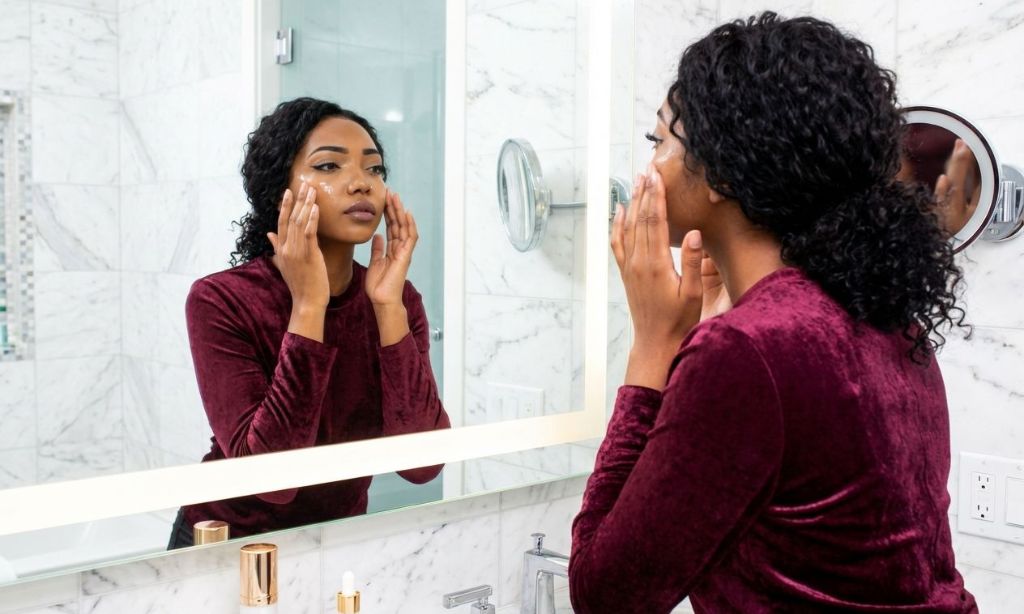 A woman applying serum to her face in a bathroom setting