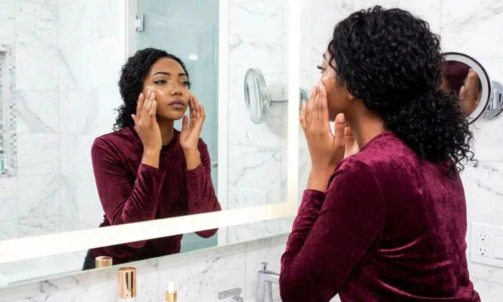A woman applying serum to her face in a bathroom setting