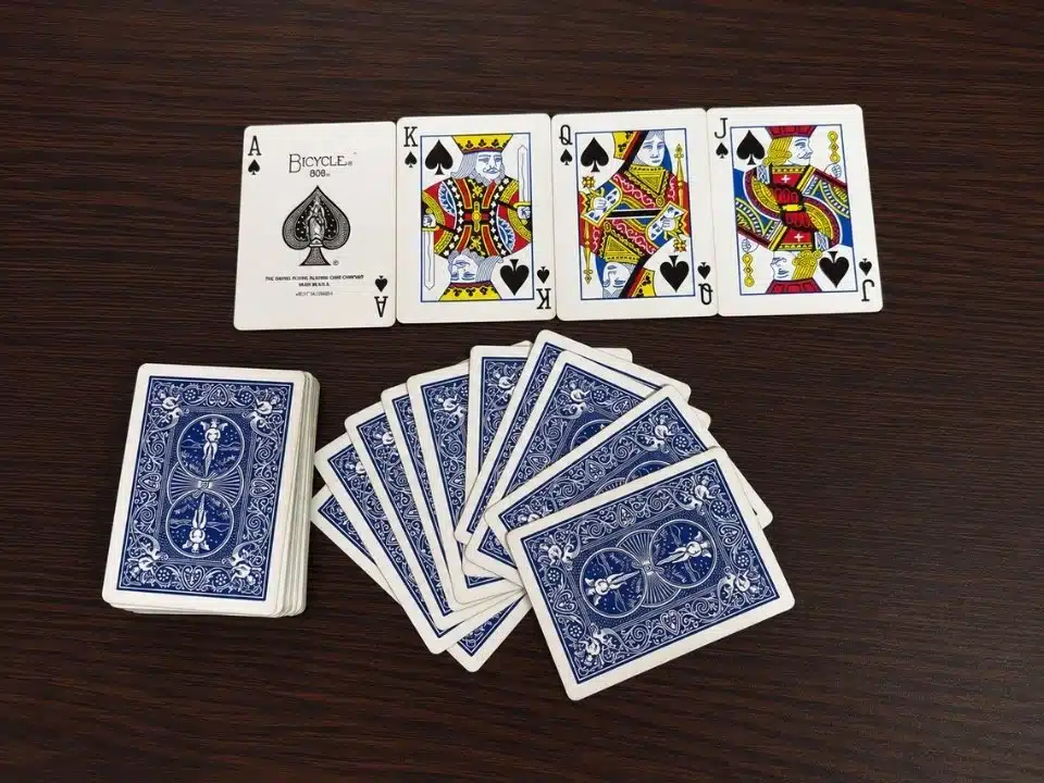 Blue backed Bicycle playing cards beside the ace, king, queen, and jack of spades on a clean wooden table.