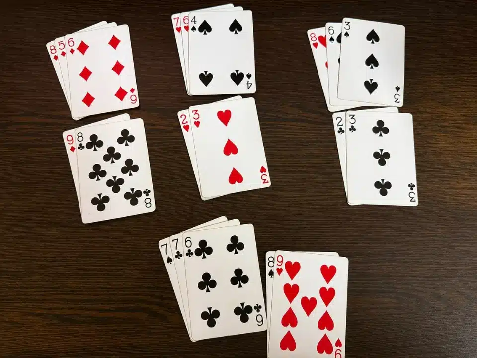 Several grouped playing cards arranged face up on a clean dark wooden table, showing different suits and values in a casual card game setup.