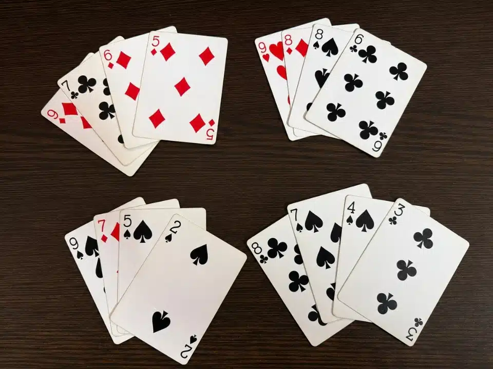Four small piles of mixed playing cards spread across a clean dark wooden surface, showing red and black suits in separate groups.